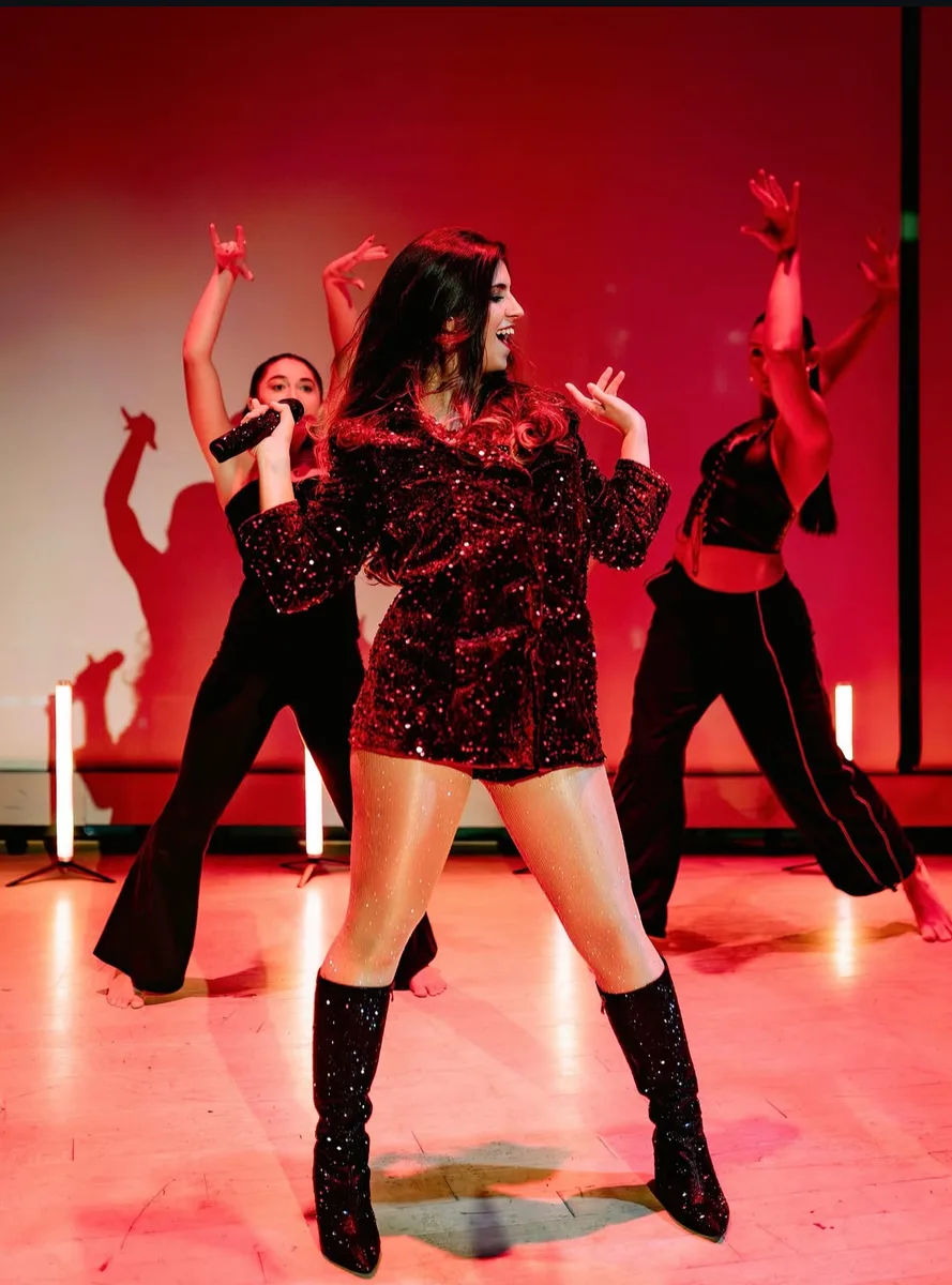 Duda performing with her dancers under red stage light to a full room